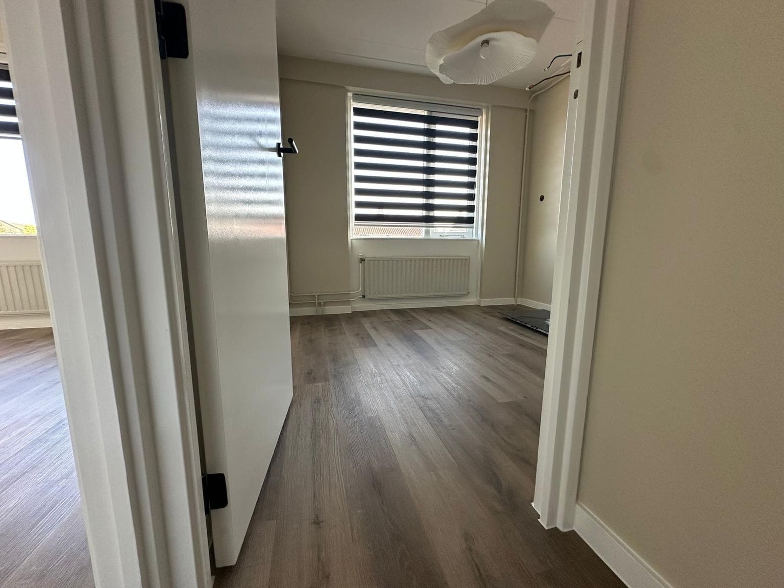 Doorkijk naar een afgewerkte kamer met donkere houten laminaatvloer en rolgordijn — Vesta Lux project in Zeeland