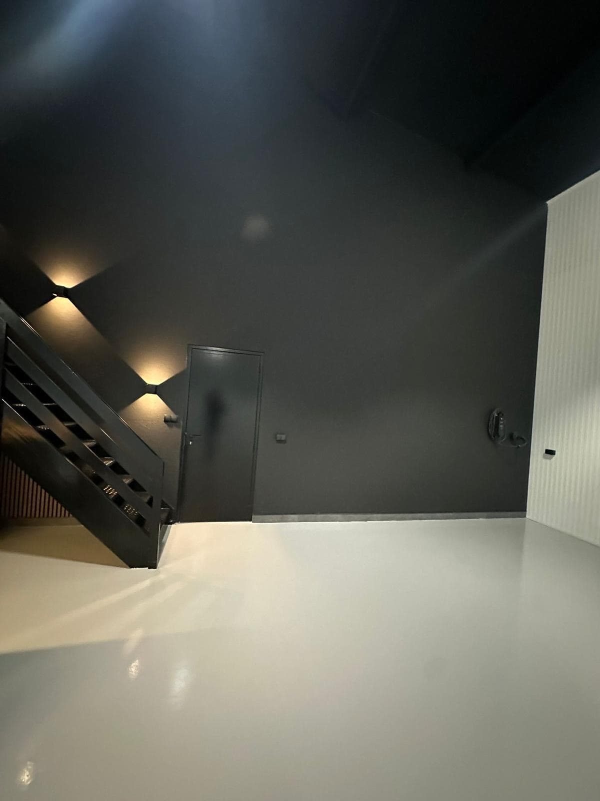 Antracietkleurige wand met zwarte trap en deur, diamant-wandlampjes en een lichte gietvloer-achtige vloer — Vesta Lux project in Zeeland